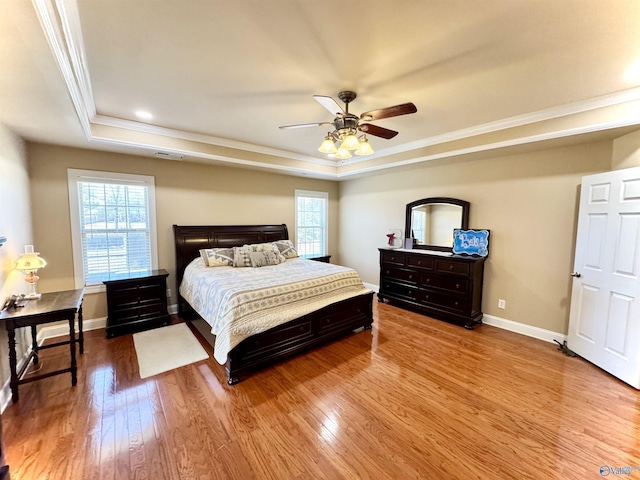 bedroom with baseboards, wood finished floors, a raised ceiling, and crown molding