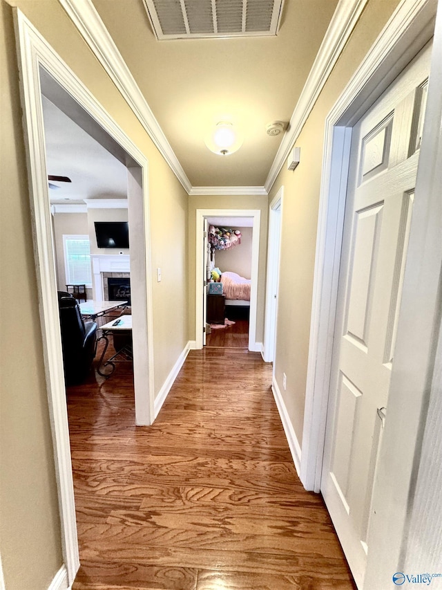 hallway featuring baseboards, visible vents, ornamental molding, and wood finished floors