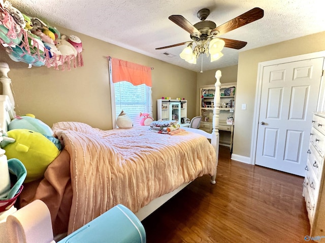 bedroom with baseboards, visible vents, a ceiling fan, dark wood-type flooring, and a textured ceiling