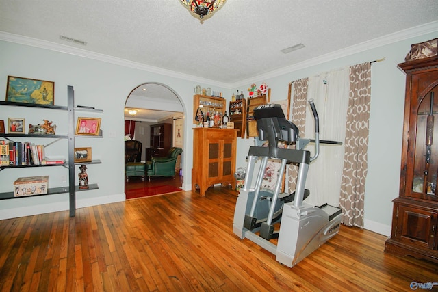 workout area with wood-type flooring, ornamental molding, and a textured ceiling