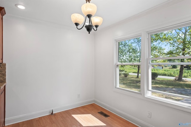 empty room featuring a chandelier, crown molding, and light wood-type flooring