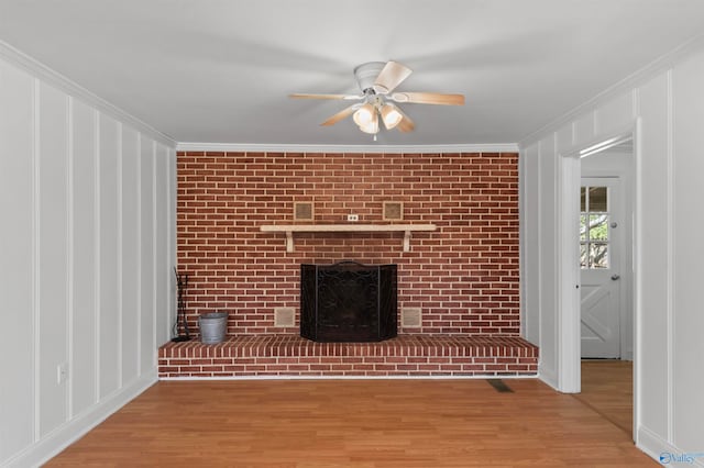 unfurnished living room with a brick fireplace, hardwood / wood-style floors, ceiling fan, brick wall, and ornamental molding