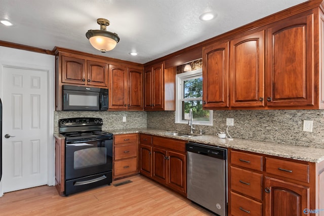 kitchen with tasteful backsplash, black appliances, sink, light wood-type flooring, and light stone counters