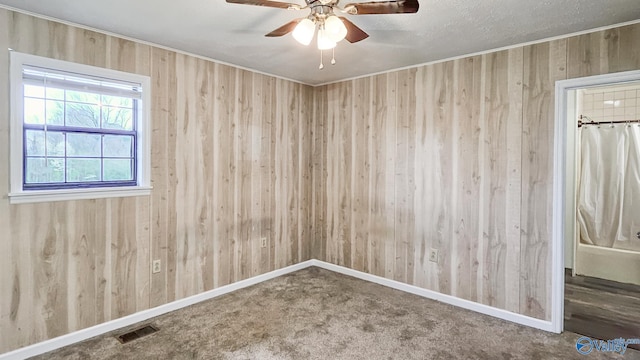 empty room with baseboards, visible vents, ceiling fan, wood walls, and carpet flooring