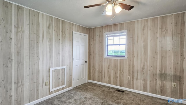 unfurnished room with wooden walls, visible vents, a ceiling fan, and carpet