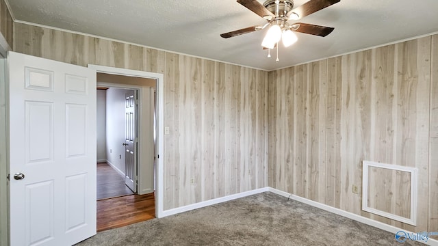 empty room featuring ceiling fan, wood walls, a textured ceiling, and carpet