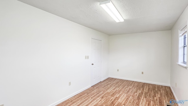 spare room with a textured ceiling, light wood-type flooring, and baseboards