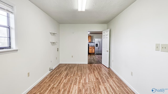 unfurnished room with a textured ceiling, light wood-type flooring, and baseboards