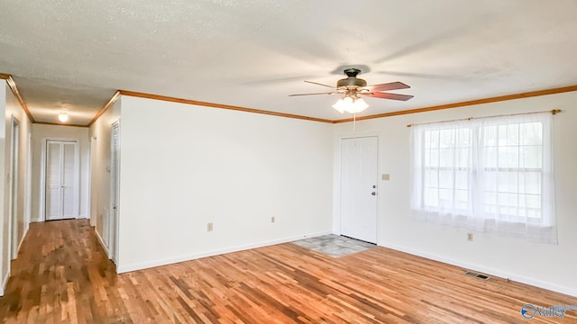 empty room with visible vents, crown molding, baseboards, wood finished floors, and a ceiling fan