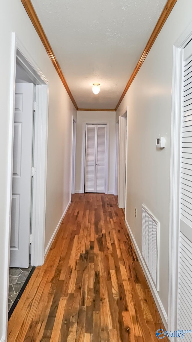 hallway with visible vents, wood-type flooring, baseboards, and crown molding