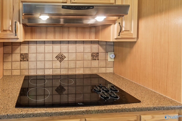 kitchen view of under cabinet range hood, black electric cooktop, backsplash, and light stone countertops
