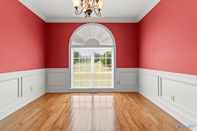 empty room with a chandelier, a wainscoted wall, light wood-type flooring, and ornamental molding