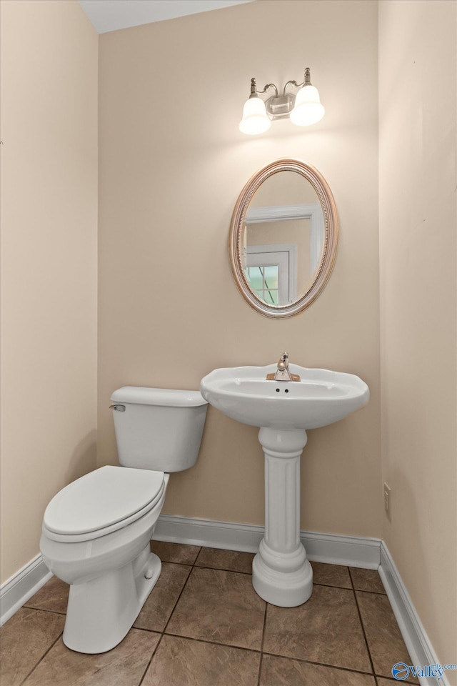 half bath featuring tile patterned floors, toilet, and baseboards