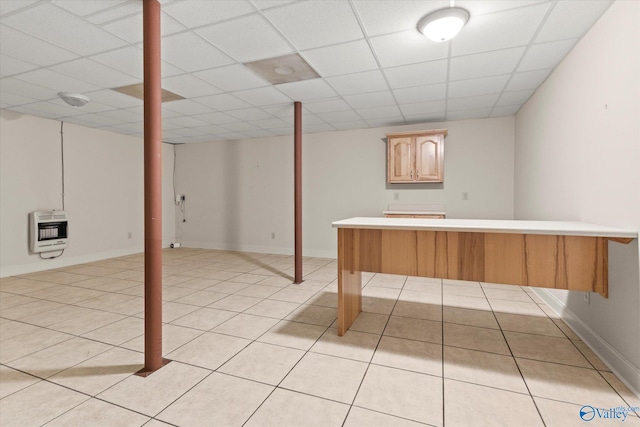 finished basement with heating unit, a drop ceiling, light tile patterned floors, and baseboards