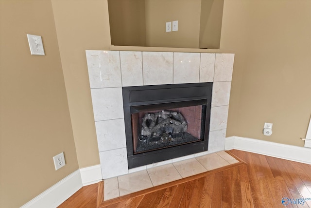 detailed view of a tile fireplace, wood finished floors, and baseboards
