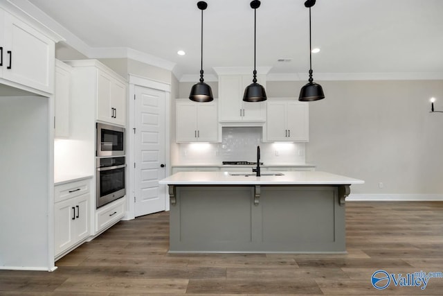 kitchen with decorative light fixtures, built in microwave, white cabinetry, an island with sink, and oven