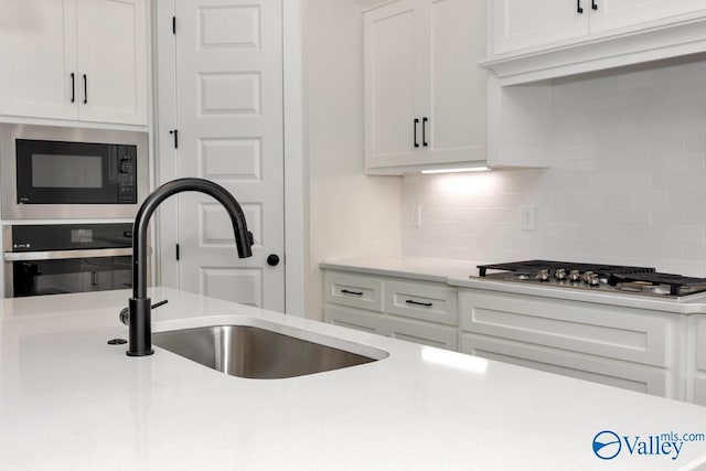 kitchen with sink, backsplash, white cabinets, and appliances with stainless steel finishes