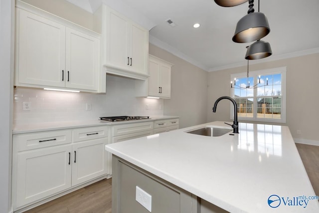 kitchen featuring stainless steel gas cooktop, sink, ornamental molding, pendant lighting, and white cabinets