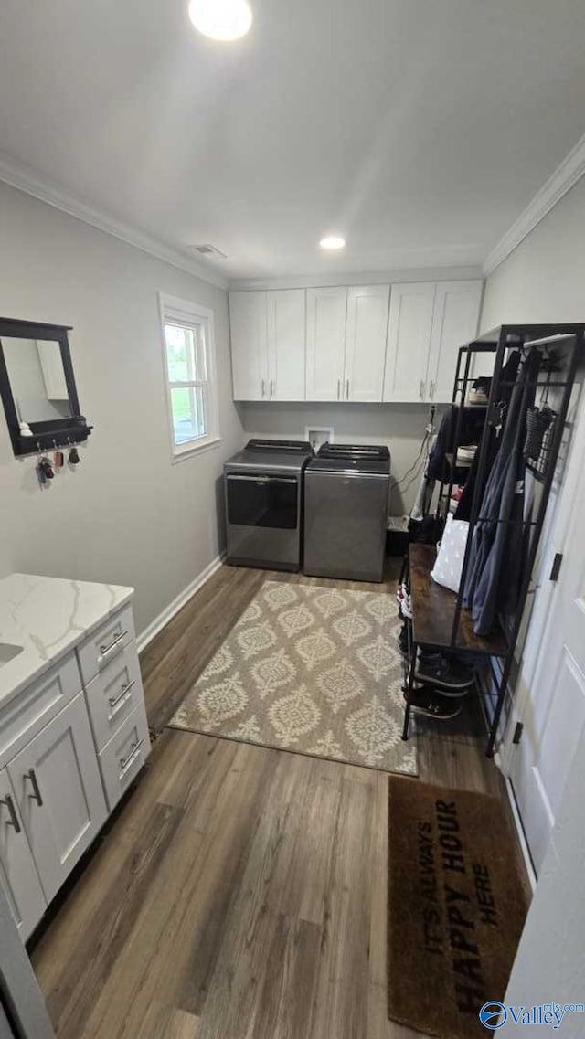 laundry area with baseboards, ornamental molding, washing machine and dryer, dark wood-type flooring, and cabinet space