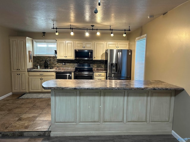 kitchen featuring backsplash, rail lighting, stainless steel appliances, sink, and cream cabinetry