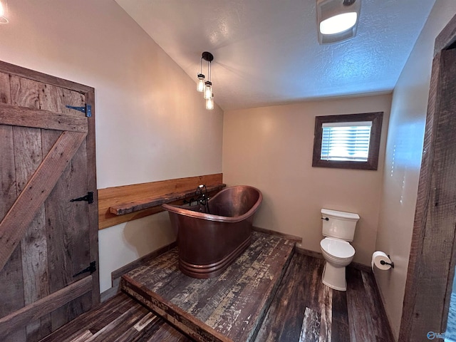 bathroom featuring hardwood / wood-style floors, lofted ceiling, a washtub, toilet, and a textured ceiling