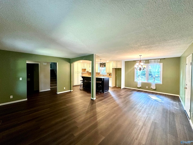 unfurnished living room featuring a notable chandelier, dark hardwood / wood-style floors, and a textured ceiling