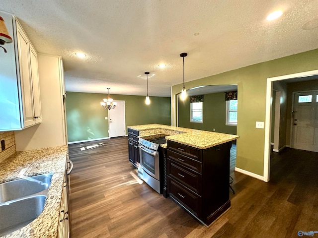 kitchen featuring stainless steel range with electric cooktop, dark wood-type flooring, light stone counters, an island with sink, and a textured ceiling