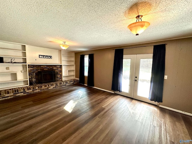 unfurnished living room with built in features, french doors, a textured ceiling, a fireplace, and dark hardwood / wood-style flooring