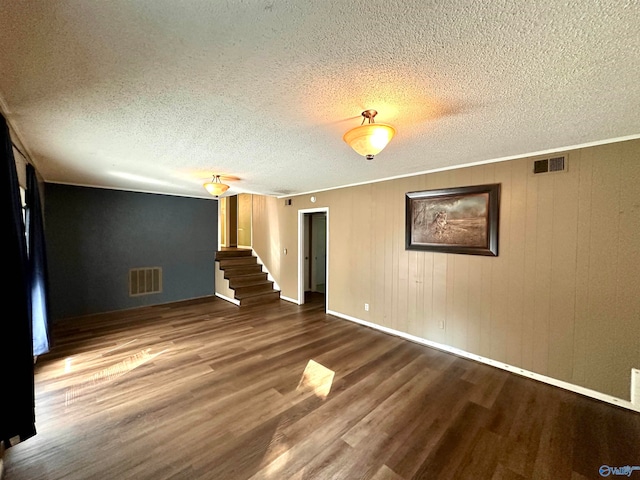 unfurnished living room with wood-type flooring, a textured ceiling, wood walls, and ornamental molding