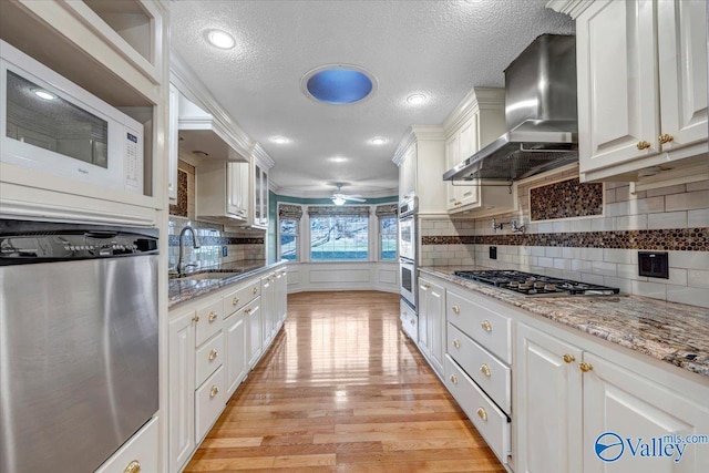 kitchen featuring stainless steel appliances, white cabinetry, a sink, and wall chimney exhaust hood