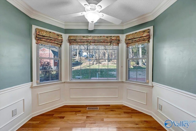 unfurnished dining area with a wainscoted wall, visible vents, a textured ceiling, and wood finished floors