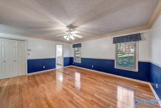 unfurnished room featuring ornamental molding, wood-type flooring, wainscoting, and a textured ceiling