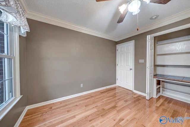 unfurnished bedroom featuring ornamental molding, light wood finished floors, a textured ceiling, and baseboards