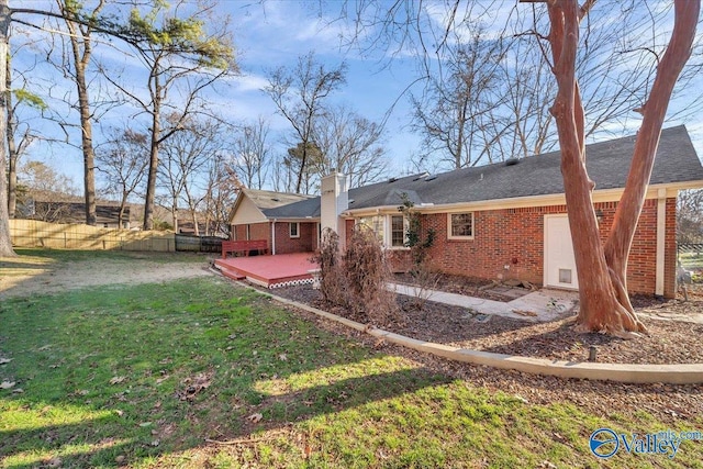 rear view of house with brick siding, fence, a lawn, a wooden deck, and a chimney