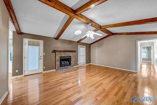 unfurnished living room featuring a textured ceiling, lofted ceiling with beams, a stone fireplace, light wood-style flooring, and baseboards