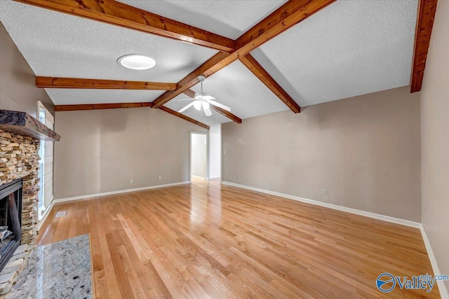 unfurnished living room with lofted ceiling with beams, a ceiling fan, light wood-style floors, a stone fireplace, and a textured ceiling