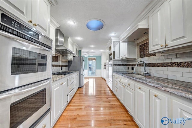 kitchen featuring wall chimney exhaust hood, a sink, white cabinetry, and stainless steel appliances