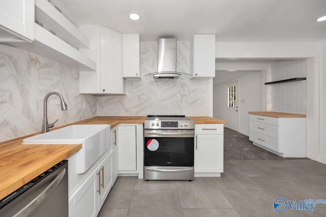 kitchen featuring wall chimney exhaust hood, butcher block counters, white cabinetry, and stainless steel appliances