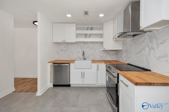 kitchen with open shelves, butcher block countertops, wall chimney exhaust hood, a sink, and appliances with stainless steel finishes
