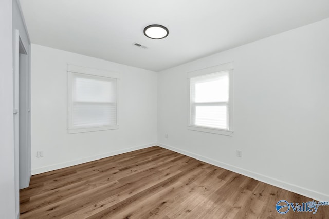 unfurnished room featuring baseboards, wood finished floors, and visible vents