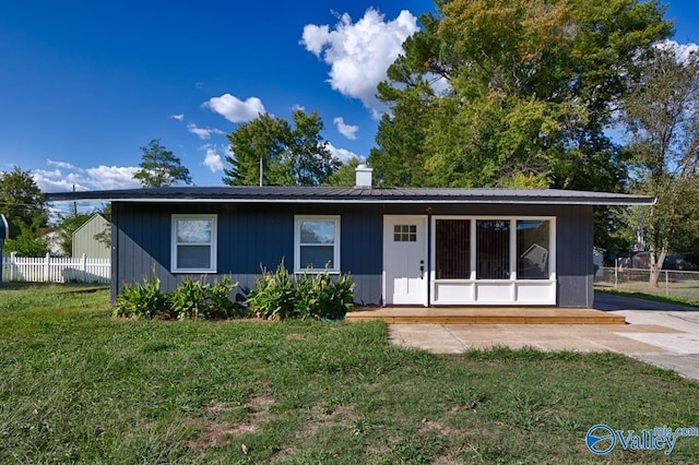 view of front of home featuring fence, a chimney, metal roof, and a front lawn