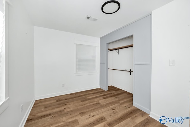 unfurnished bedroom with baseboards, a closet, wood finished floors, and visible vents