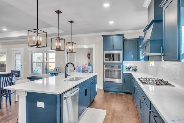 kitchen featuring appliances with stainless steel finishes, sink, hanging light fixtures, blue cabinetry, and a center island with sink