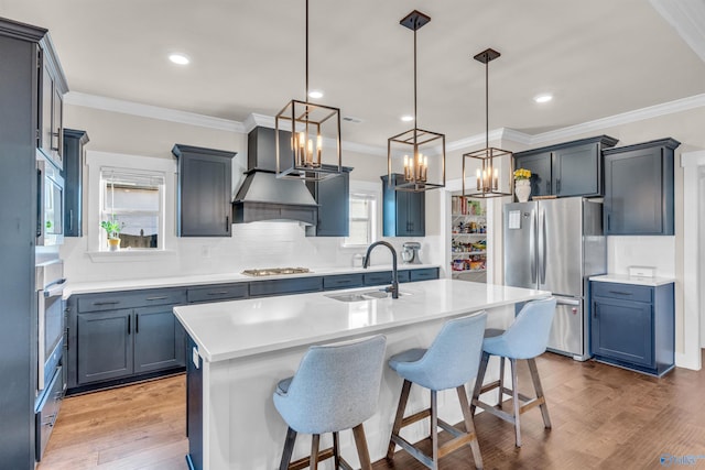 kitchen featuring hanging light fixtures, a kitchen breakfast bar, stainless steel appliances, an island with sink, and custom range hood