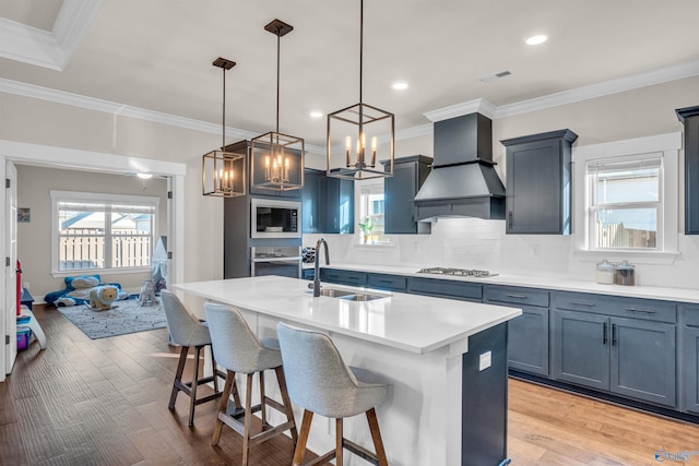 kitchen with premium range hood, sink, appliances with stainless steel finishes, pendant lighting, and a kitchen island with sink