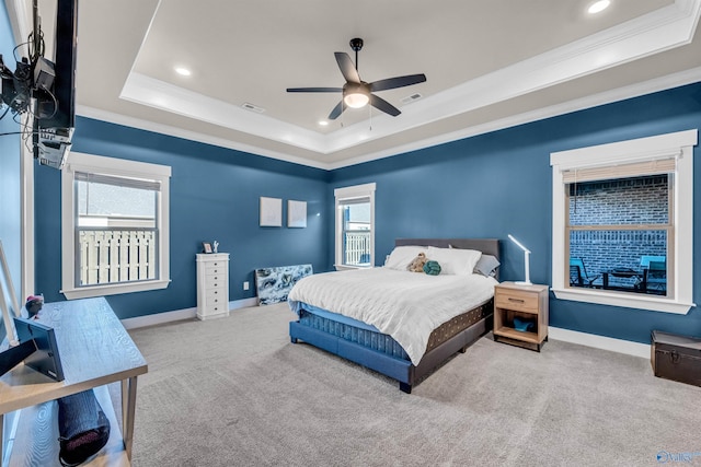 carpeted bedroom with multiple windows, a tray ceiling, ornamental molding, and ceiling fan