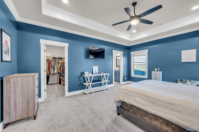 bedroom with a tray ceiling, a walk in closet, ornamental molding, and light colored carpet