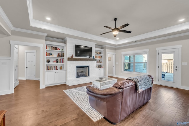 living room with hardwood / wood-style floors, a fireplace, ceiling fan, a tray ceiling, and crown molding