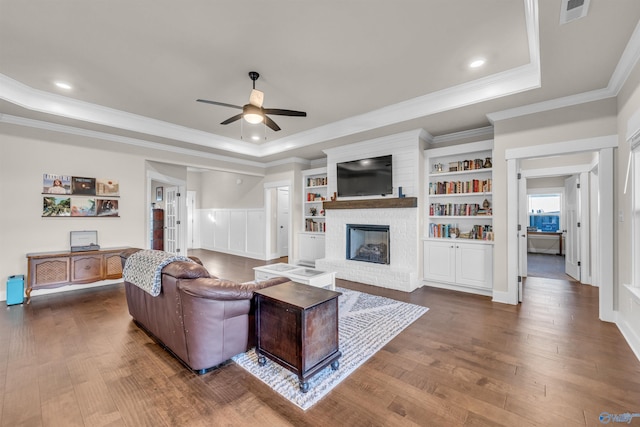 living room featuring a raised ceiling, a brick fireplace, hardwood / wood-style flooring, and ceiling fan