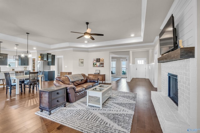 living room featuring dark wood-type flooring, ceiling fan, ornamental molding, and a tray ceiling